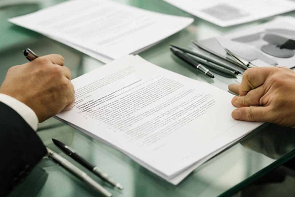 Avvocato che annota clausole contrattuali su un tavolo di vetro con documenti ordinati
